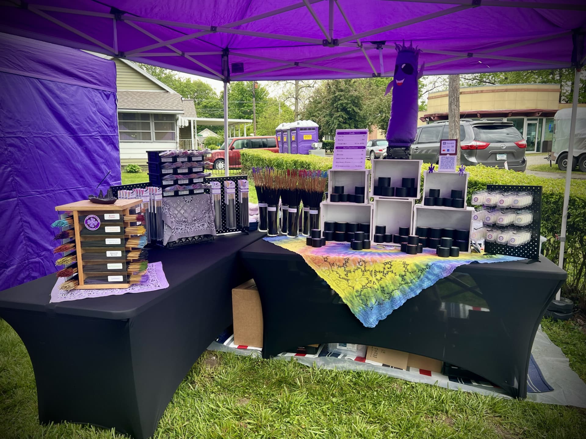 Purple Clover Incense vendor booth under a purple canopy with black-draped tables holding incense, candles in crates, and wax melts at MayFest 2026 in Camp Chesterfield, Indiana